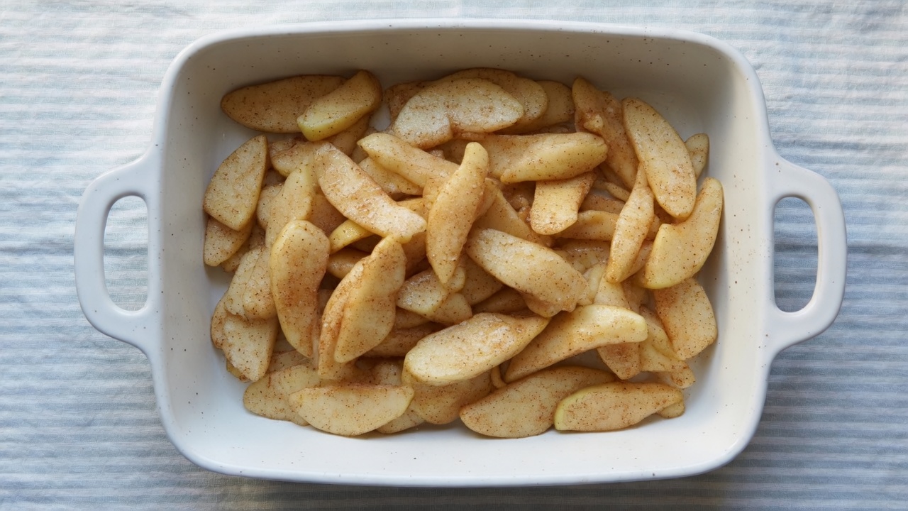 Peeled apple slices tossed with sugar in the baking dish