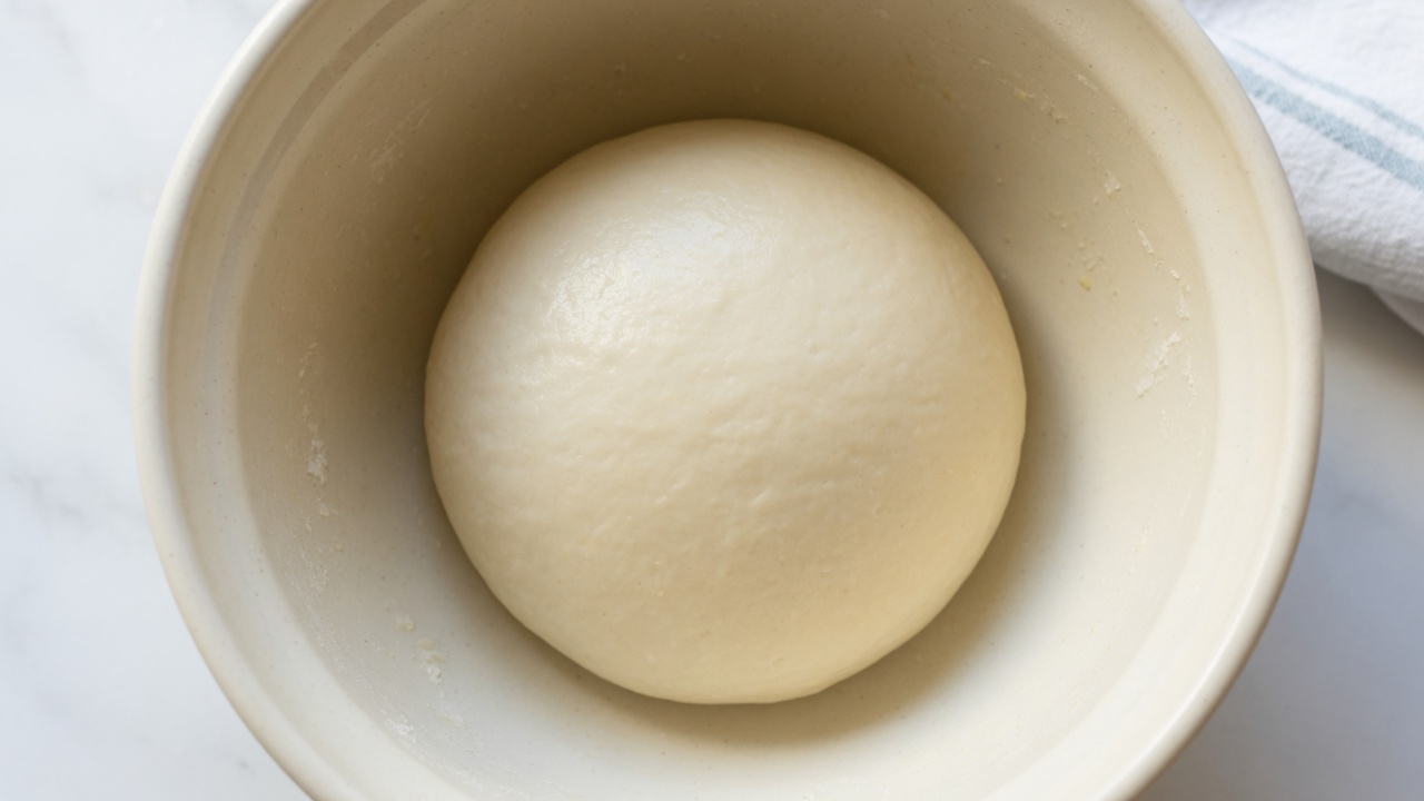 Smooth risen bagel dough ball in a bowl