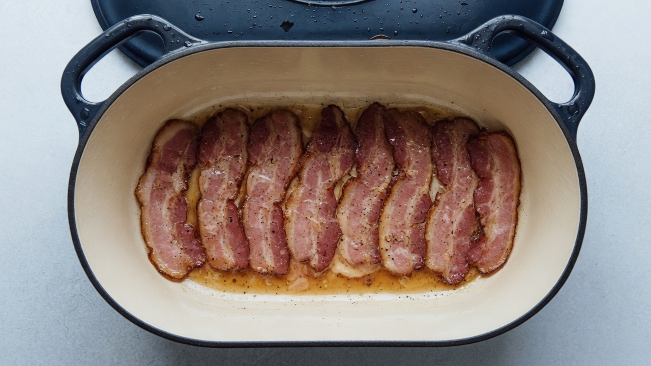 Bacon cooking in a navy Dutch oven with cream interior