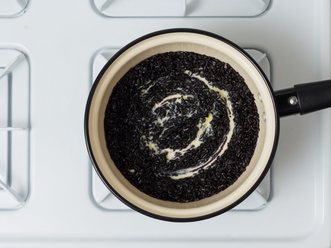Black rice stirring in melted butter in a cream enamel saucepan