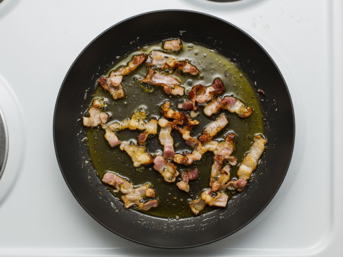 Bacon cooking in a wide black carbon-steel skillet with olive oil